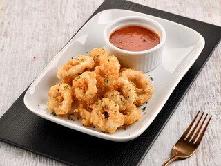 CALAMARI FRITTI or Fried Squid Rings with chilli sauce served in dish isolated on wooden table side view of italian fast food