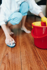 Woman cleaning wooden floor with bucket and mop, red bucket and red mop in the background