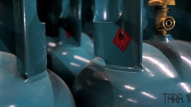 Flammable! modern blue-green gas cylinders close-up
A close-up shows a propane gas cylinder valve and its warning label indicating flammable contents. The setting highlights safety measures for gas st
