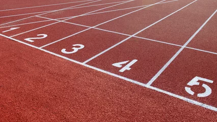 Selbstklebende Fototapeten Numbers on the red running track of the garden. Starting field for sprint at the stadium. White stripes and numbers on the red track, close-up. Running track at the stadium for competitions. © aneriksson