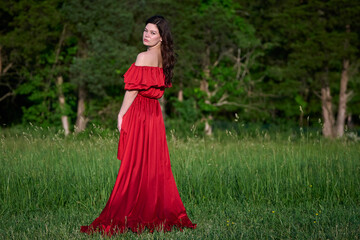 Fototapeta premium Sexy woman in beautiful red dress stands in open field - fashion