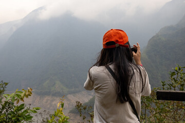 female traveler taking photos of amazing landscape with mountains and cloudy sky over a reservoir with a smartphone during vacation