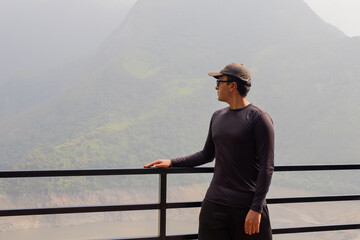 Traveler man in a cap contemplating a landscape with mountains and a reservoir after hiking on...