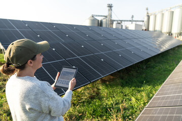 Female farmer with digital tablet on a modern farm using solar panels. Agricultural silos in the...