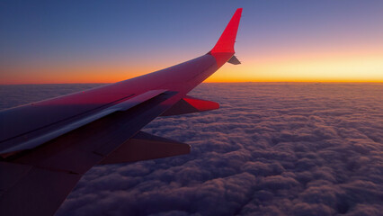 Fototapeta premium Airplane Wing Above Clouds During Vibrant Sunset at High Altitude