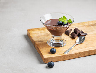 Chocolate pudding in a glass with fresh blueberries and mint on a wooden board on a light background