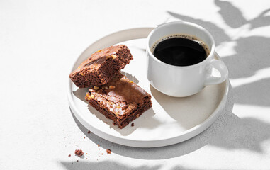 Pieces of chocolate brownie with nuts on a plate with a cup of espresso coffee on a light background