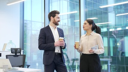 Two colleagues engaged in friendly conversation with coffee in modern office setting. Co-workers, a man and a woman have a casual discussion. Teamwork, effective communication and collaboration