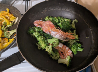 Cooking shrimp on a bed of broccoli with colorful bell peppers in a kitchen setting