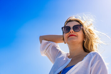 Portrait of beautiful smiling middle-aged woman in sunglasses against blue sky background