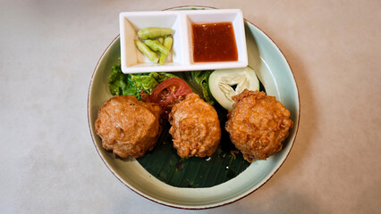 Crispy Fried Perkedel Tahu Served with Fresh Vegetables and Sweet Chili Sauce on a Banana Leaf Lined Plate
