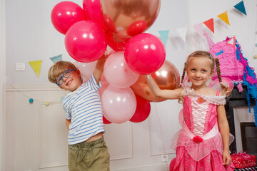 Brother and sister hold many pink balloons at birthday party