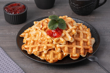 Delicious waffles topped with strawberry jam on a black plate with a grey wooden background