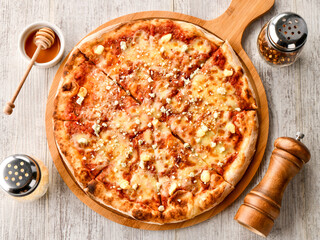 Hawaiian Pizza topping of melted cheese and a drizzle of honey served on a rustic wooden board, alongside honey, pepper flakes, and a pepper grinder top view of fast food