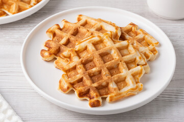 Crispy golden waffles served on a round white plate in a cozy kitchen setting