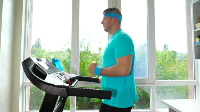 Cardio training on a treadmill with 1 kg dumbbells in your hands. A young man runs on a treadmill at home. Slow motion. Weight loss concept.