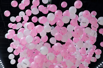 many balloons on a dark background, a lot of white and pink balloons fall from the ceiling. The balloons are floating, vibrant colors and the sheer number of balloons create a festive atmosphere