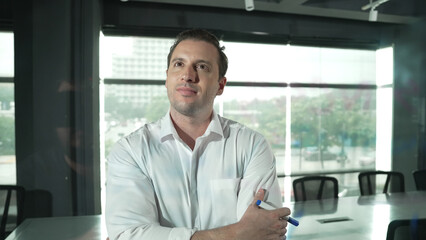 Fototapeta premium Smart businessman thinking about start up project in front of glass board. Smiling male project manager looking at colorful sticky notes with show creativity marketing strategy. Manipulator.