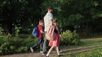 happy family. father leads children by hand school. boy girl child with school backpacks rush lesson. caring dad with his daughter son are walking around school yard. happy family concept. teamwork