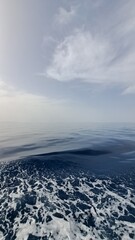 A close-up shot of choppy ocean water creates a dynamic foreground of white foam against a smooth expanse of blue, with a hazy sky above, evoking a sense of movement, energy, the vastness of the sea