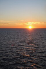 Die Sonne ist schon halb untergegangen über dem Skagerrak an einem Sommerabend im Juli. Das Abendlicht ist orange über dem Horizont. Ein paar Sonnenstrahlen werden vom dunklen Wasser reflektiert.