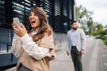 Fototapeta premium Excited businesswoman receiving good news on smartphone in front of office building