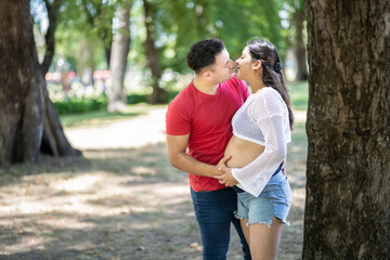 Fototapeta premium Pregnant latin couple about to kiss in a park