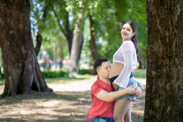 Fototapeta premium Latin man kissing his pregnant wife's belly in a beautiful park