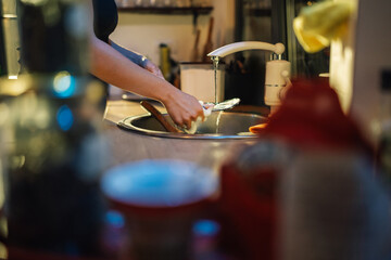 Woman washing dishes in kitchen sink with running water