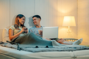 Lesbian couple relaxing in bed, drinking coffee and watching movie on laptop