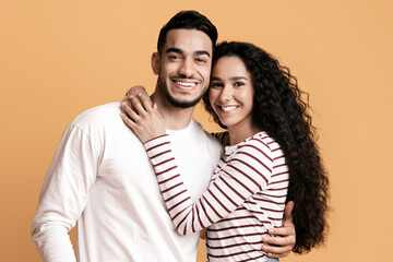 Obraz premium Romantic Couple. Portrait Of Happy Young Middle Eastern Man And Woman Embracing On Yellow Background, Cheerful Millennial Arab Spouses Hugging And Smiling At Camera While Posing In Studio, Free Space