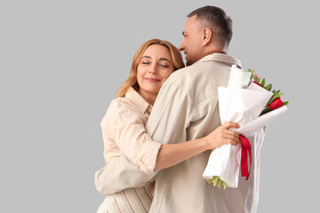 Middle-aged couple with bouquet of flowers on grey background. International Women's Day
