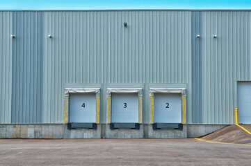 Side view of a building with three industrial loading docks. Each dock has a closed blue roll-up door and is equipped with an extendable dock leveler at the base.