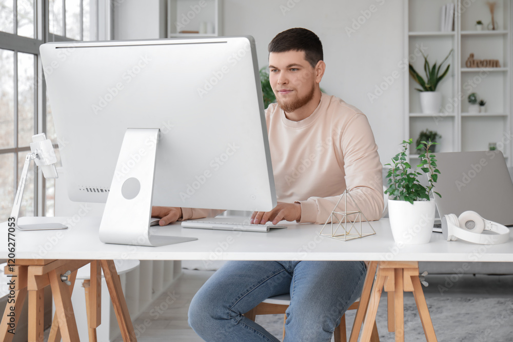 Poster young bearded man using computer on table at home