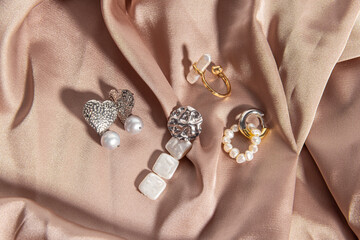 Various accessories made of natural pearls on pink silk background. Rings and earrings