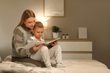 Mother reading story to her little son in bedroom at night