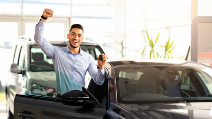 Emotional middle eastern guy buying car of his dream, happy male customer standing by nice shiny...