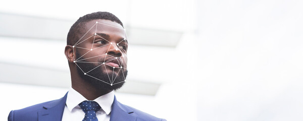 A man in a blue suit stands confidently, with a facial recognition overlay superimposed on his face. This advanced technology highlights the growing use of ID verification in various environments.