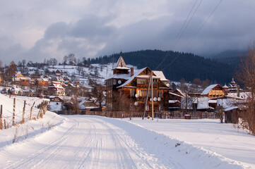 Fototapeta premium A picturesque winter scene in the Ukrainian Carpathian Mountains featuring a snow-covered village with traditional wooden houses. The image captures the serene beauty of a winter landscape
