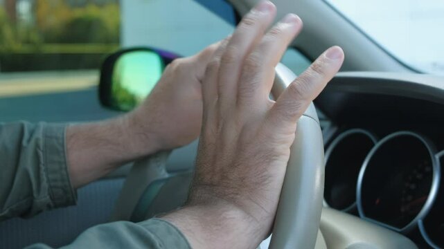 Close-up of a nervous man's hands on the steering wheel of a car. The man hits the steering wheel with his fingers and honks his horn furiously. Concept of rush, car traffic jam, traffic jam.
