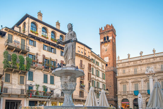 Italian square with fountain and Lamberti clock tower and classic architecture with ancient buildings in Verona, Veneto, Italy. Piazza delle Erbe with Fontana di Madonna. Tourist destination