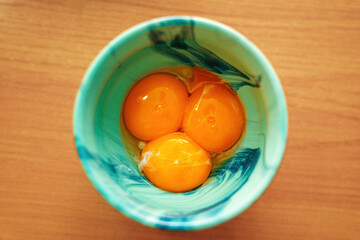 vibrant green ceramic round bowl filled with three chicken egg yolks, one of which has spilled. Ideal for culinary, cooking, and food photography