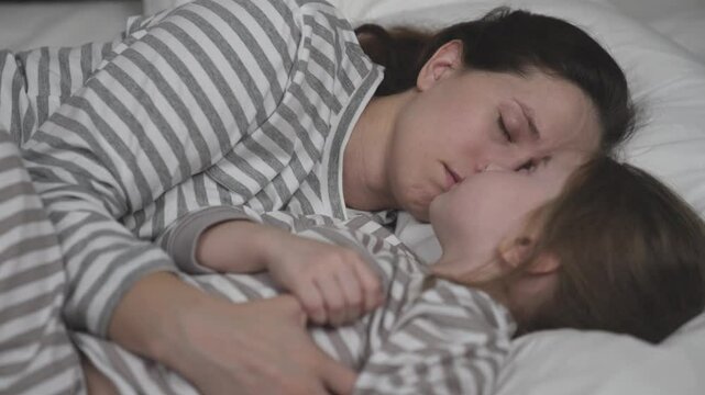 Brunette mother and little child sleep bed together. Mom and daughter lean cheeks hugging tightly. Woman and kid see sweet dreams cozy bedroom. Happy family. Children sleep with plush toy and mommy.