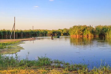 Summer sunny landscape. Fisherman on a boat preparing for fishing on the Blue Lake with reeds