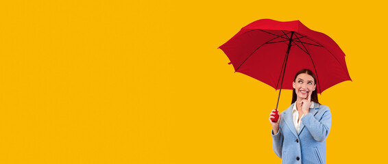 Full length portrait of dreamy lady standing under yellow umbrella at studio, thinking and looking...
