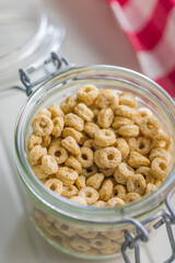Sweet honey cereal rings in jar on white table.