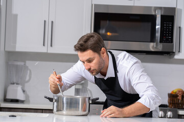modern chef in professional uniform. close-up on the hand of male chef who is stirring soup in pot...
