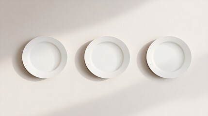 Three empty white plates hanging on a beige wall creating shadows