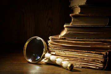 Magnifying glass with ancient books on wooden table. Pile of a very old books.
