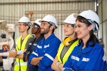 Team of diverse workers wearing safety gear stands confidently in a modern industrial facility